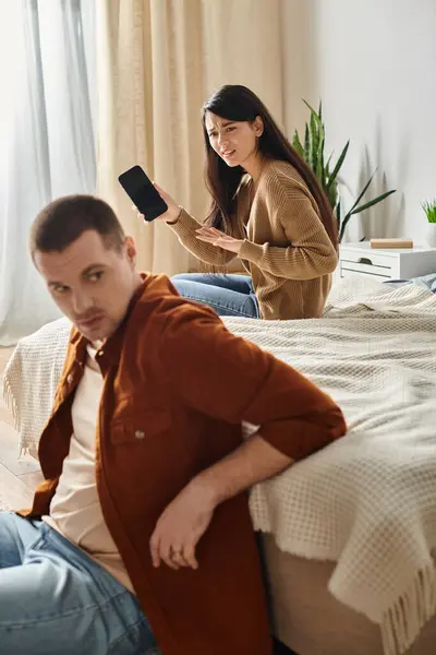 Irritated asian woman with mobile phone looking at young  husband in bedroom at home, family trouble — Stock Photo