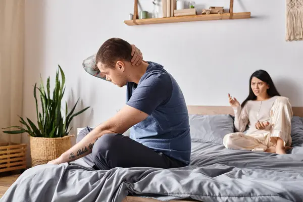 Angry asian woman quarreling at upset husband sitting on bed at home, relationship difficulties — Stock Photo
