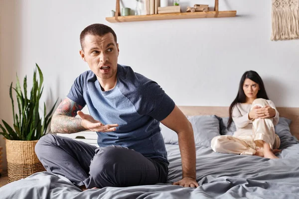 Young irritated man quarreling at upset asian woman sitting on bed at home, divorce concept — Stock Photo