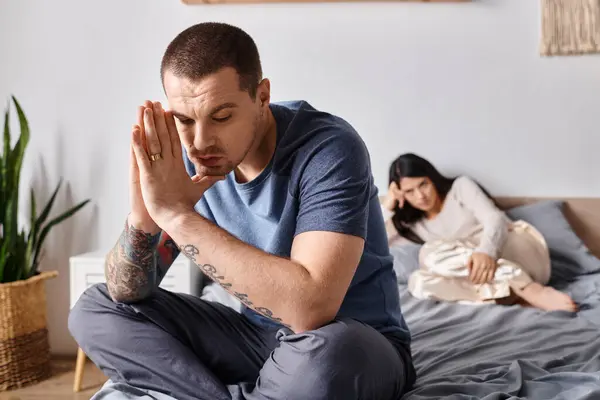 Giovane depresso tatuato uomo seduto sul letto vicino offeso asiatico moglie, famiglia divorzio concetto — Foto stock