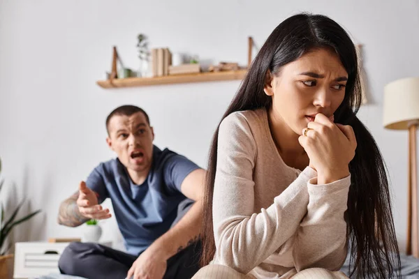 Young depressed asian woman sitting near angry husband in quarrelling in bedroom, divorce concept — Stock Photo