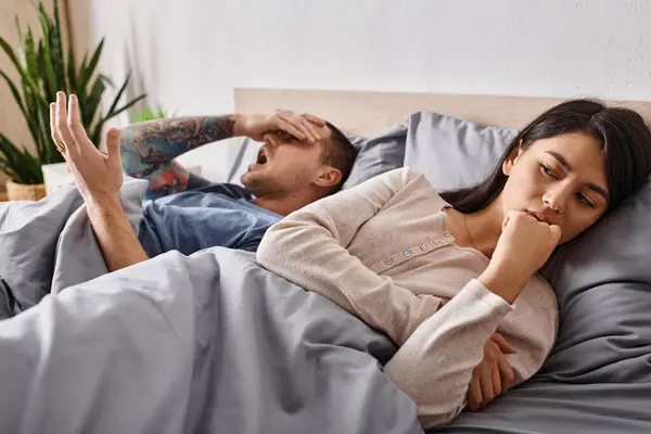 Young frustrated asian woman lying down on bed near quarrelling husband, relationship conflict — Stock Photo