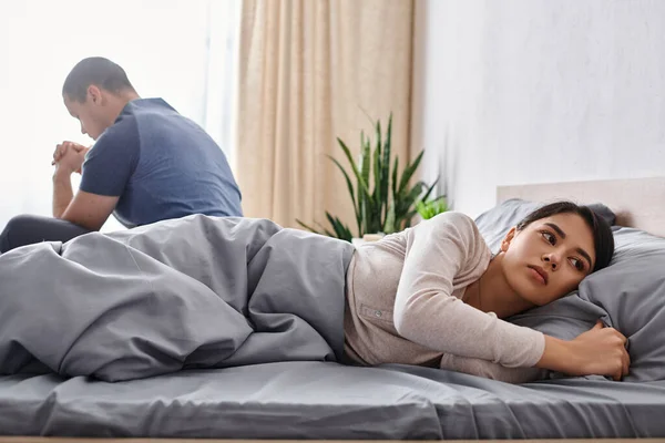 Sconvolto donna asiatica guardando lontano vicino marito seduto sul letto a casa, difficoltà di relazione — Foto stock