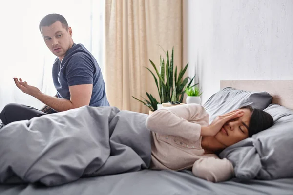Giovane uomo parlando con frustrato asiatico moglie oscurare faccia su letto a casa, rapporto difficoltà — Foto stock
