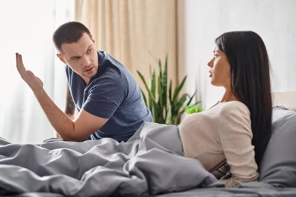 Uomo emotivo parlando con offeso asiatico moglie mentre seduta su letto a casa, rapporto difficoltà — Foto stock