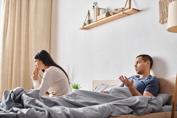 Giovane uomo parlando con offeso asiatico donna mentre sdraiato in camera da letto, rapporto problemi — Foto stock