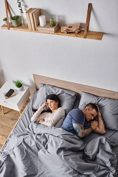 Vista ad alto angolo di frustrata coppia multiculturale sdraiata sul letto a casa, problemi familiari — Foto stock
