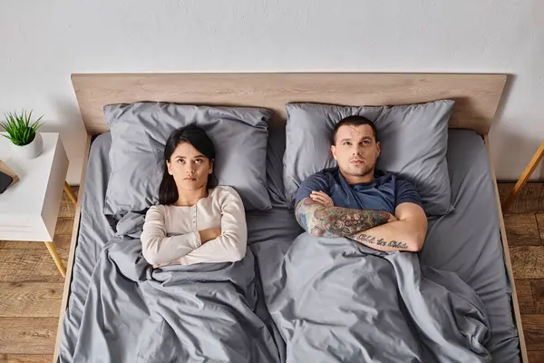 Vue de dessus de jeune couple multiculturel frustré couché avec les bras croisés sur le lit à la maison — Photo de stock