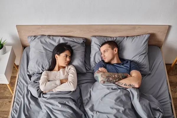 Vista superior de la pareja interracial ofendido acostado en la cama y mirándose, conflicto - foto de stock