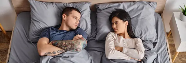 Vista superior de jovem chateado casal interracial deitado na cama e olhando um para o outro, banner — Fotografia de Stock
