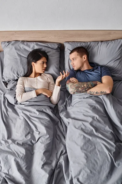 Vue de dessus de jeune couple interracial couché avec les bras croisés et se quereller sur le lit à la maison — Photo de stock