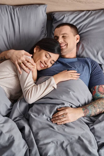 Top view of young joyful multicultural couple embracing in bedroom at home, family happiness — Stock Photo