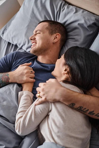Top view of young overjoyed interracial couple embracing in bedroom at home, family happiness — Stock Photo