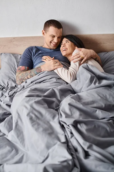 Joven pareja multiétnica abrazando y riendo en el dormitorio en casa, confianza y comprensión - foto de stock