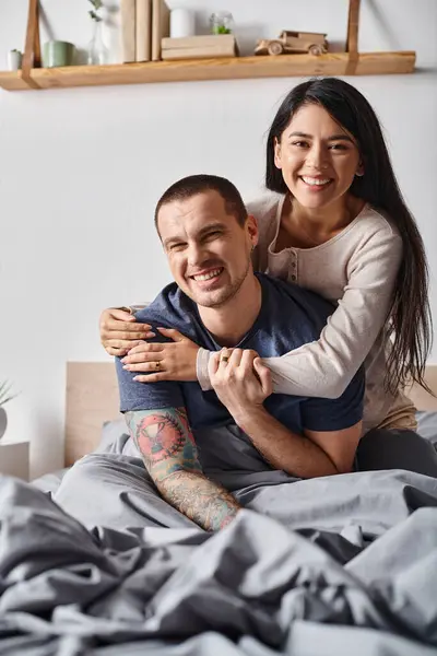 Alegre casal multicultural abraçando e olhando para a câmera no quarto em casa, alegria e felicidade — Fotografia de Stock