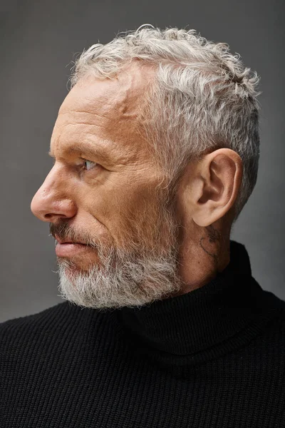 Handsome fashionable mature man in stylish black turtleneck posing and looking away on gray backdrop — Stock Photo