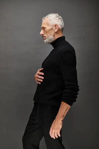 Bel homme mature à la mode à col roulé noir élégant posant et regardant loin sur fond gris — Photo de stock