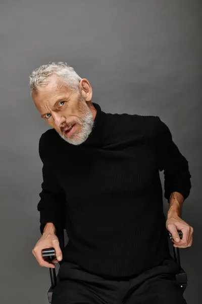 Appealing mature man with beard in voguish turtleneck sitting on folding chair and looking at camera — Stock Photo