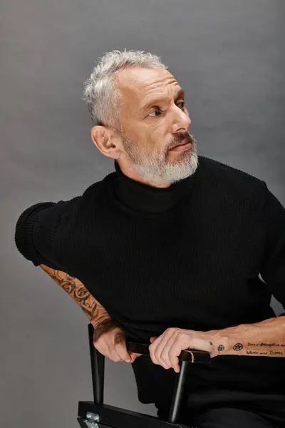 Atraente modelo masculino maduro em gola alta na moda sentado na cadeira dobrável e olhando para longe — Fotografia de Stock
