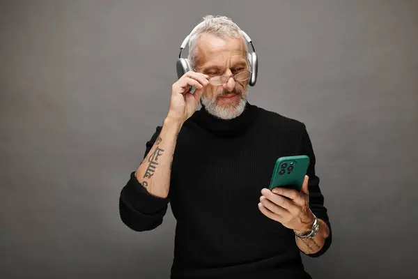 Gut aussehende männliche Modell mit Bart und Kopfhörer in schwarzem Rollkragen Blick auf Handy — Stockfoto