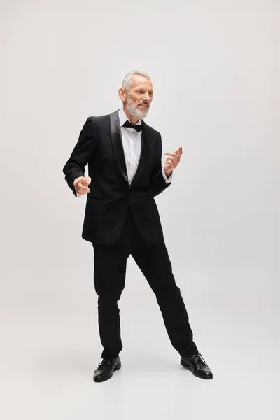 Handsome cheerful mature man with gray beard and bow tie in elegant tuxedo dancing actively — Stock Photo