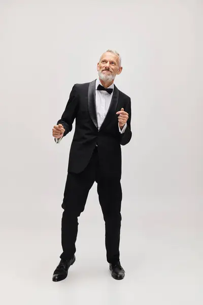 Guapo hombre maduro alegre con barba gris y pajarita en elegante esmoquin bailando activamente - foto de stock