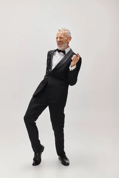 Homem maduro alegre de boa aparência com barba cinza e laço em elegante smoking dançando ativamente — Fotografia de Stock