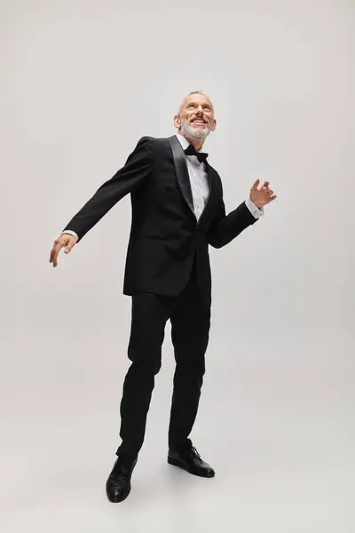 Good looking joyous mature man with gray beard and bow tie in elegant tuxedo dancing actively — Stock Photo