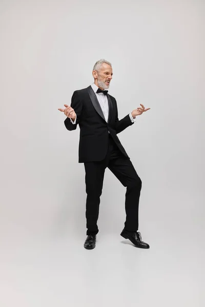 Beau joyeux homme mature avec barbe grise et noeud papillon dans élégant smoking dansant activement — Photo de stock