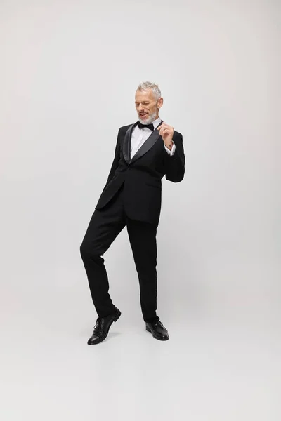 Appealing merry mature male model with gray beard and bow tie in elegant tuxedo dancing actively — Stock Photo