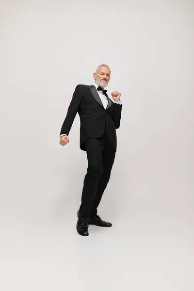 Attractive happy mature man with gray beard and bow tie in elegant tuxedo dancing actively — Stock Photo