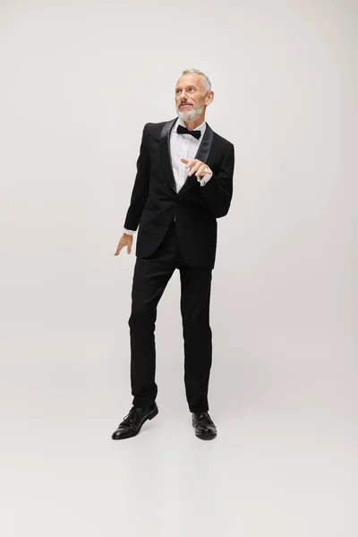 Well dressed mature male model with bow tie in chic black tuxedo dancing actively on gray backdrop — Stock Photo