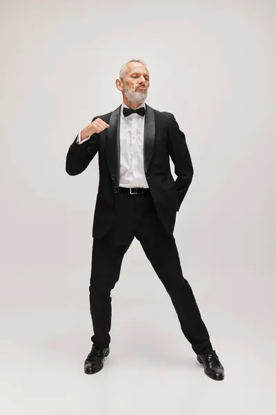 Atractivo barbudo hombre maduro en debonair esmoquin negro con pajarita posando en movimiento mientras baila - foto de stock