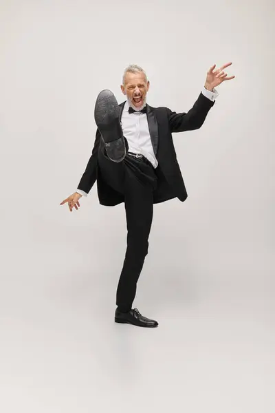 Alegre bom olhar homem maduro em terno elegante com gravata borboleta dançando feliz no fundo cinza — Fotografia de Stock
