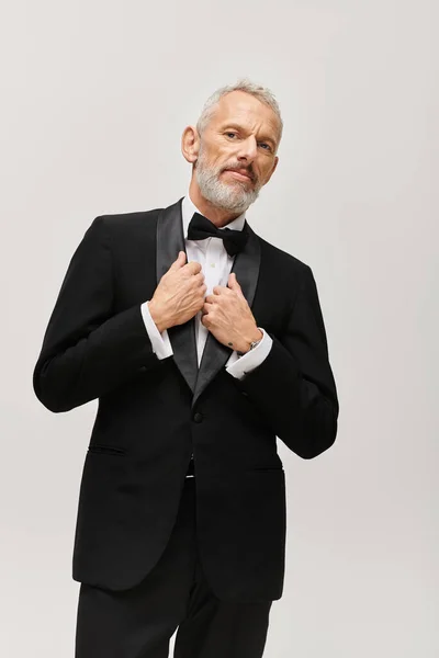 Hombre barbudo maduro con corbata de lazo en elegante esmoquin posando y mirando a la cámara - foto de stock