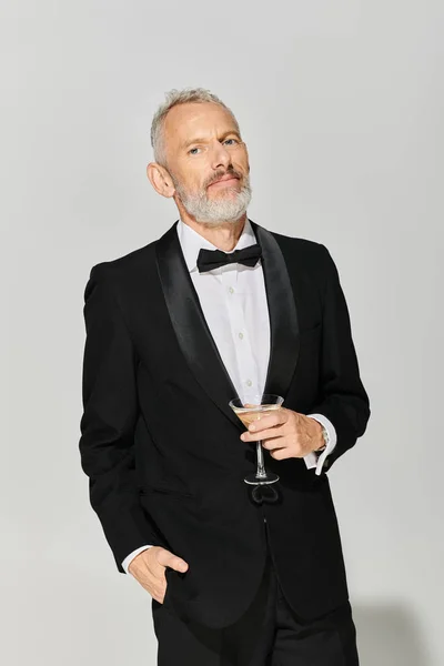 Handsome bearded mature male model  in elegant tuxedo holding martini glass and looking at camera — Stock Photo