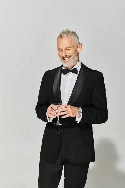 Homem maduro bonito alegre em smoking chique com barba cinza sorrindo e segurando martini com azeitonas — Fotografia de Stock
