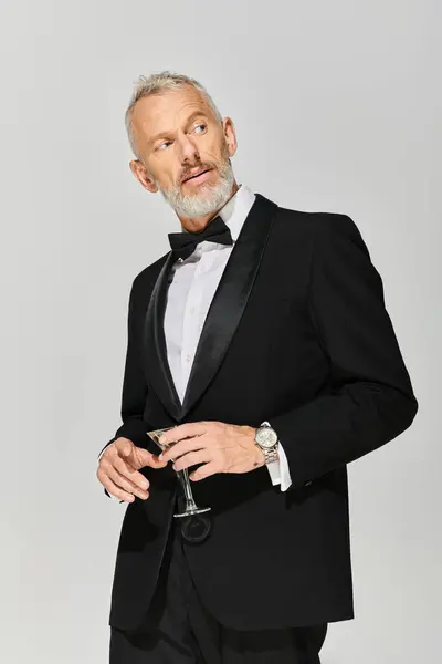 Handsome bearded mature man in elegant tuxedo with bow tie holding martini and looking away — Stock Photo