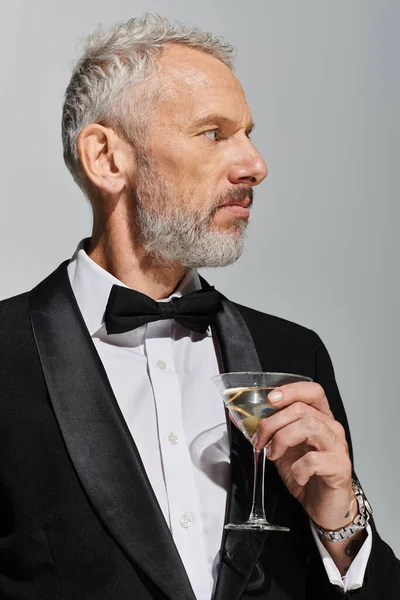 Atraente barbudo maduro homem no elegante smoking com laço gravata segurando martini e olhando para longe — Fotografia de Stock