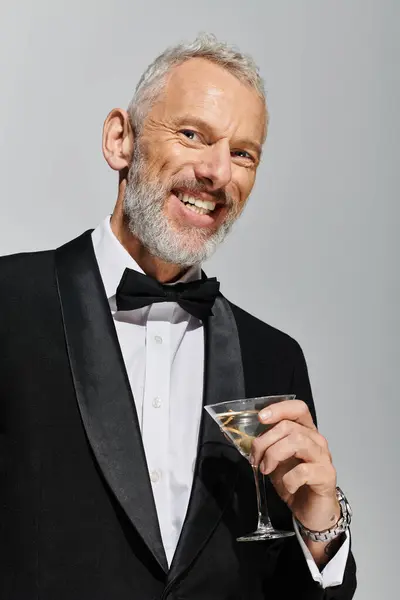 Allegro uomo maturo dall'aspetto gradevole in elegante smoking che regge un bicchiere di martini e sorride alla macchina fotografica — Foto stock