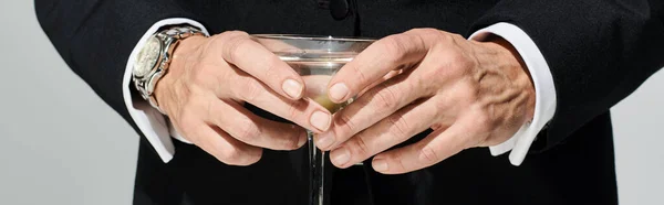 Abgeschnittene Ansicht des Glases von leckeren Martini mit grünen Oliven in den Händen eines reifen Mannes, Banner — Stockfoto