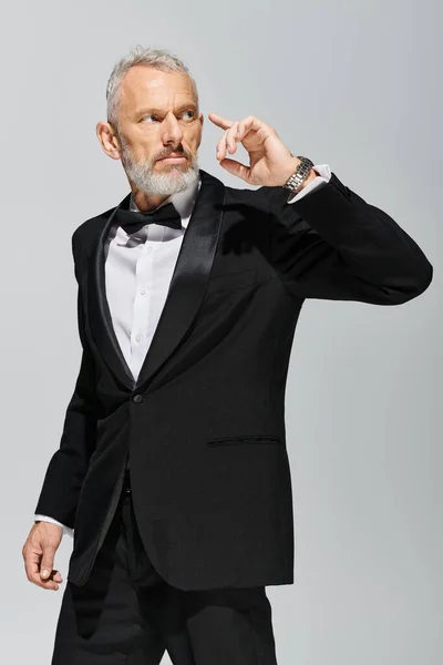 Schöner, eleganter, reifer Mann mit Bart trägt modischen Smoking mit Fliege und schaut weg — Stockfoto