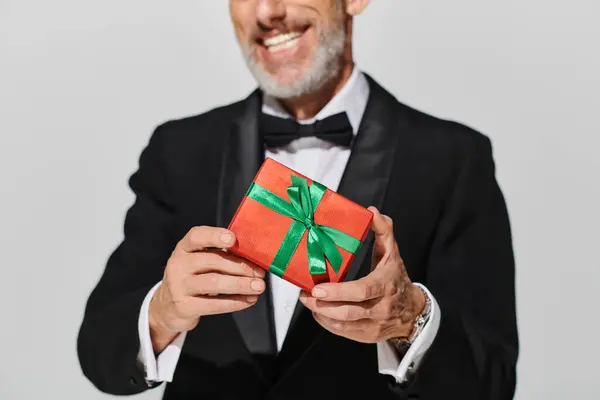 Cropped view of fashionable elegant mature man with beard in tuxedo holding present in hands — Stock Photo