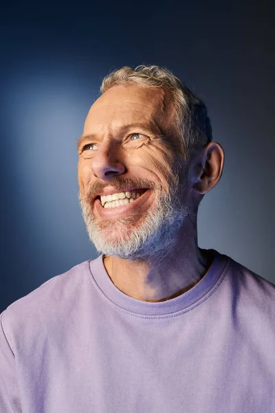 Cheerful bearded mature man in casual purple sweatshirt with accessories smiling and looking away — Stock Photo