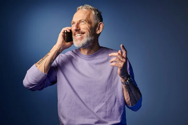 Joyeux barbu branché mature homme en violet élégant sweat-shirt parler par téléphone sur fond bleu — Photo de stock