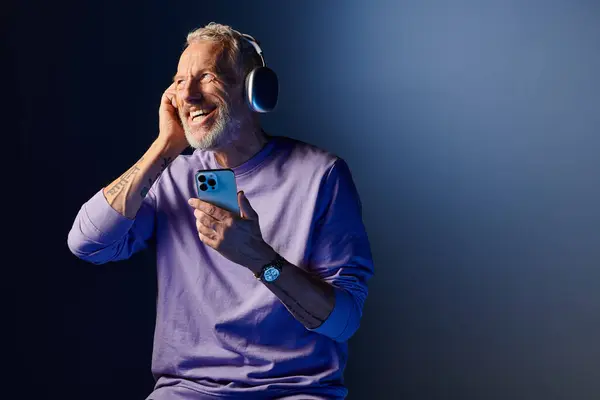 Gut aussehender, reifer Mann mit Bart und Kopfhörer, der Musik genießt und auf sein Handy schaut — Stockfoto