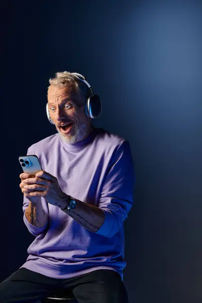 Joyful surprised mature man with beard and headphones enjoying music and looking at his phone — Stock Photo