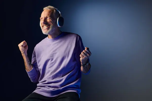 Gioioso uomo maturo attraente con barba grigia e cuffie in felpa viola godendo della musica — Foto stock