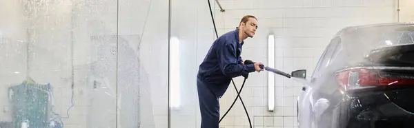 Bom olhar trabalhador trabalhador serviceman em uniforme azul usando mangueira para lavar carro moderno preto, banner — Fotografia de Stock