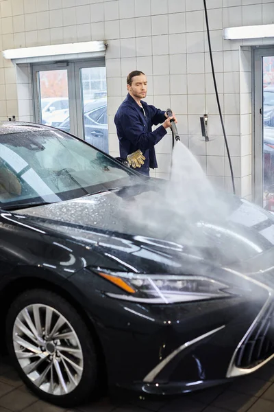 Ansprechende hart arbeitende Profis in Uniform mit gesammelten Haaren, die modernes schwarzes Auto waschen — Stockfoto